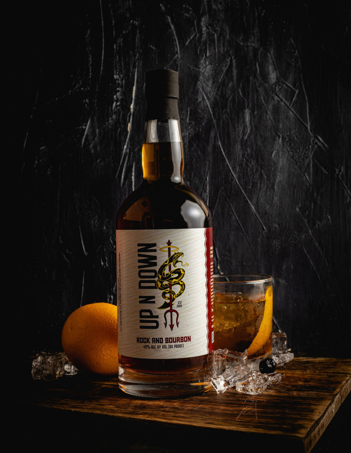 Up N Down Rock & Bourbon bottle on a wood board with ice, orange and a poured Old Fashioned
